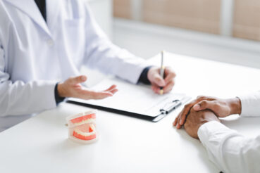 Dentist explaining endodontic treatment to patient in office Dentist holding a tooth model for examination and research 歯科衛生士が麻酔の認定を取得するまでの流れ